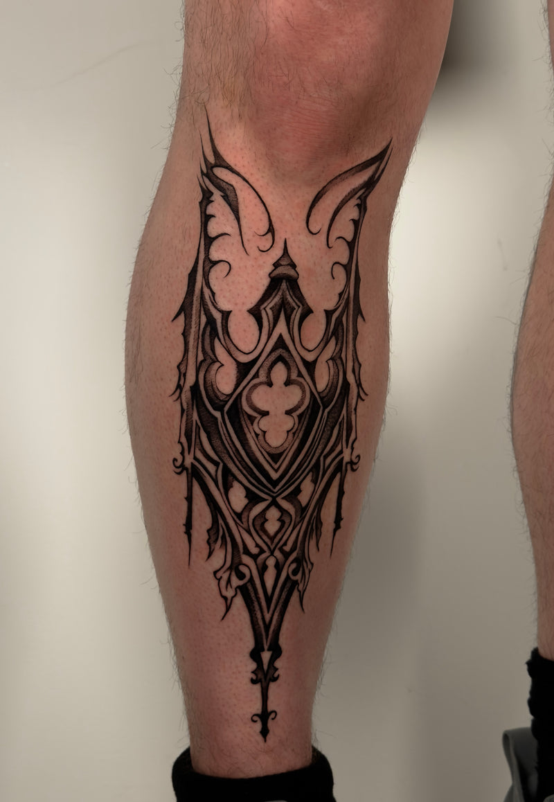A close-up of a person's lower leg featuring a detailed black gothic architecture tattoo
