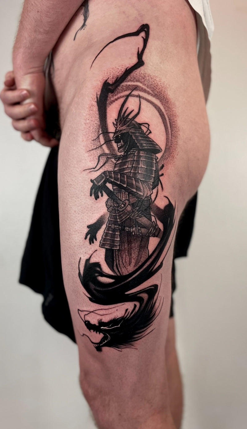 A large black and gray tattoo of a samurai warrior with flowing brush-like elements on a person's upper thigh, shown against a plain light background.