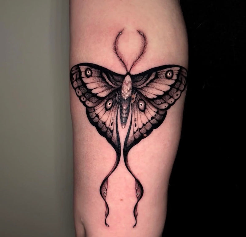 A detailed black and gray tattoo of a large moth applied to a person's upper arm.