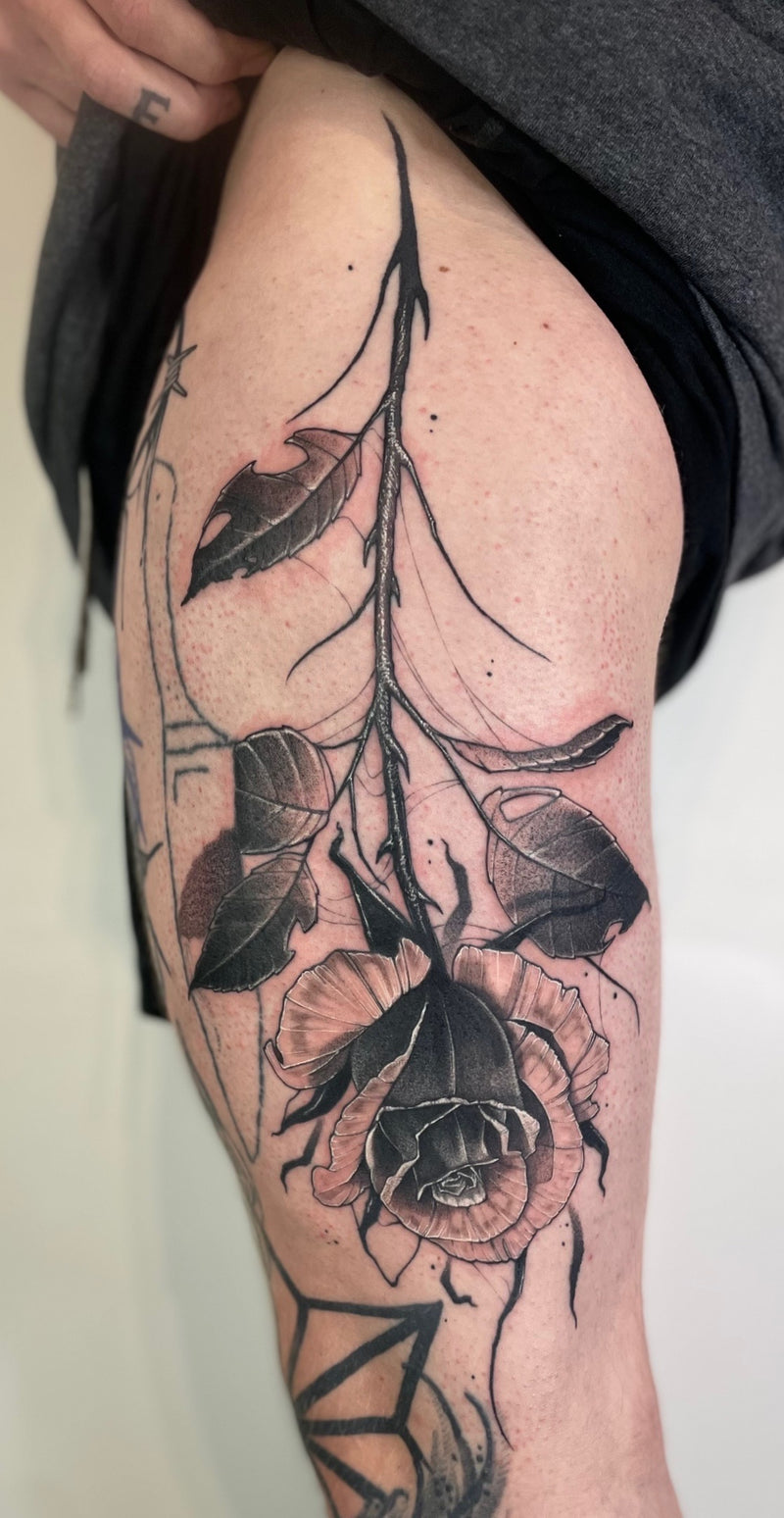 A close-up of a person's thigh showing a large black and gray rose tattoo 