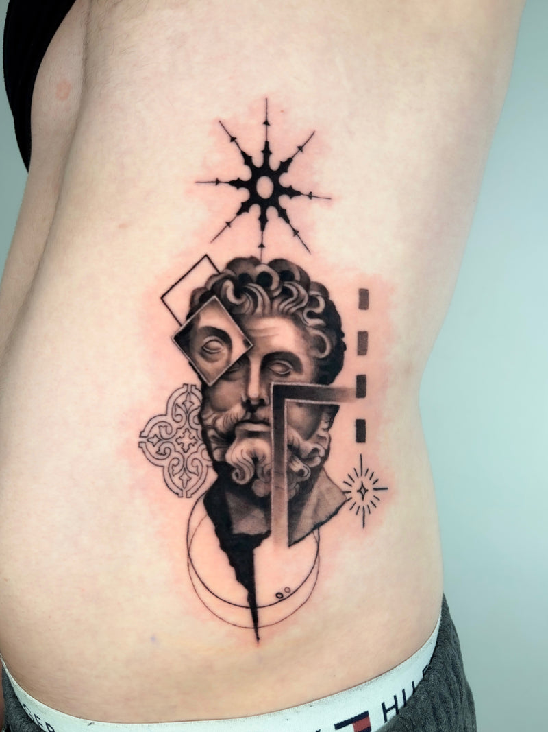 A black and gray geometric tattoo of a classical bust with abstract shapes and a starburst, shown on a person's lower back or hip.