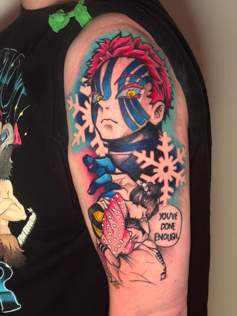A close-up of a colorful anime tattoo on a person's upper arm, featuring Tanjiro Kamado from Demon Slayer with red hair, blue markings, snowflakes, and a pink-haired character with the text 'YOU'VE DONE ENOUGH!'. The person is wearing a black sleeveless top.