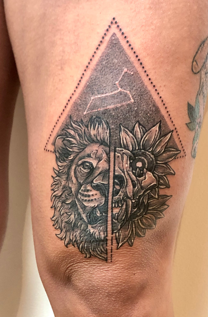 A close-up of a person's thigh featuring a detailed black and gray tattoo of a split lion and sunflower design inside a dotted triangle.