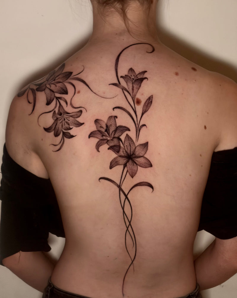 A person shown from the back wearing a black off-the-shoulder top, displaying a large floral tattoo on their upper back and shoulders in black and dark gray ink.
