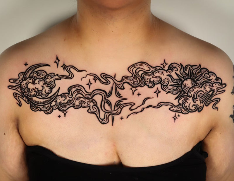 A black woodcut style chest tattoo featuring a crescent moon, clouds, stars, and a sun design on a person's upper chest.
