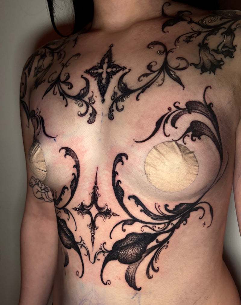 A close-up of a person's chest and upper torso showing a large black ornamental floral tattoo design across the skin.