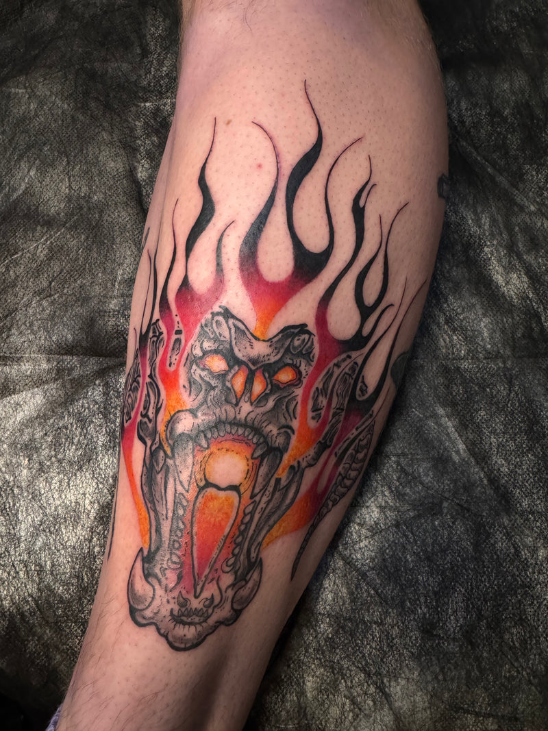 A close-up of a freshly tattooed forearm featuring a detailed black, red, and orange skull surrounded by bold flames.