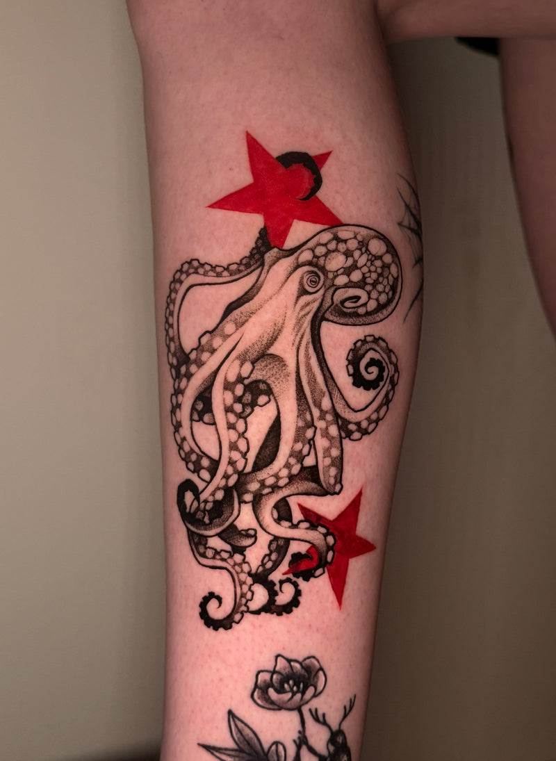 A close-up of a person's calf featuring a black ink octopus tattoo with two bold red star accents 