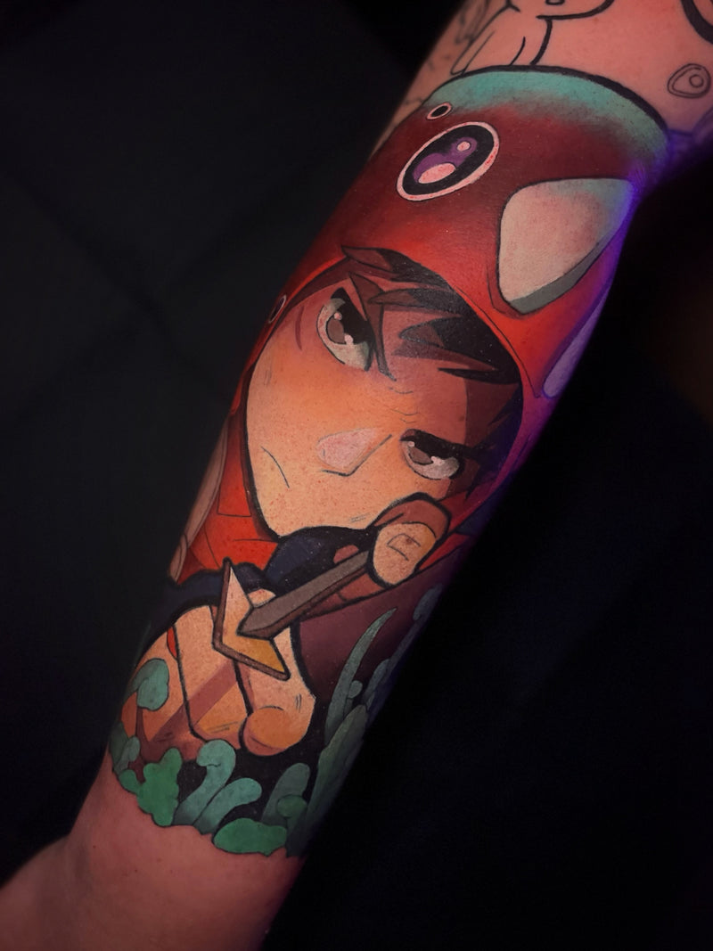 A close-up of a tattoo on a person's forearm featuring a stylized anime character wearing a red cap, with green and orange details, done by Kelsie.