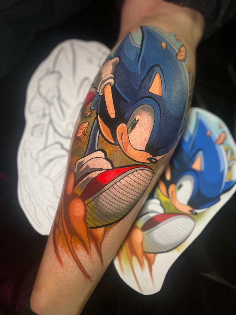 A close-up of a person's forearm featuring a colorful hand-drawn style Sonic the Hedgehog tattoo, done by Kelsie.
