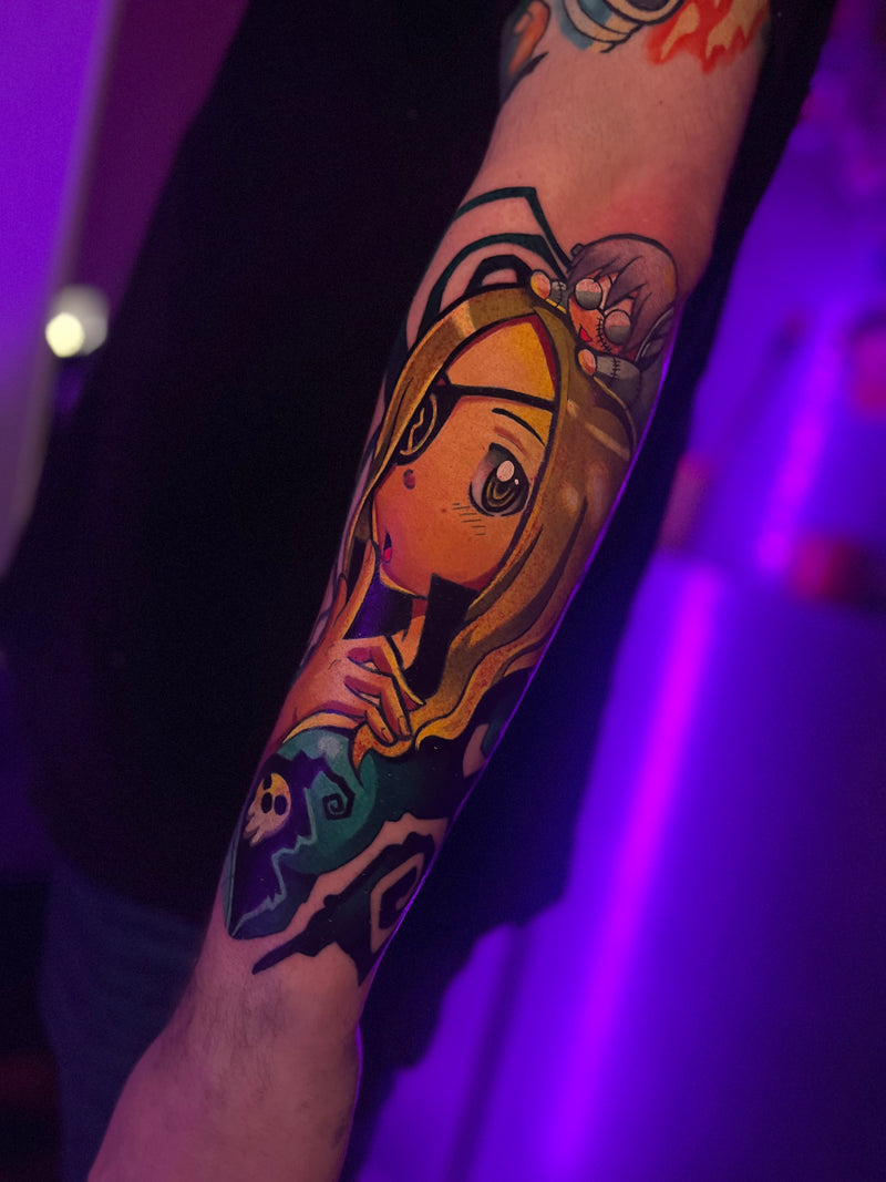 A close-up of a person's forearm featuring a colorful anime-style tattoo with a blonde character, done by Kelsie.