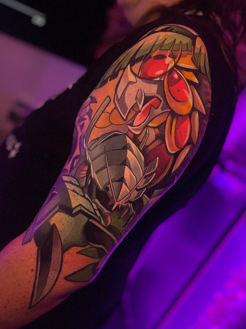 A close-up of a person's upper arm featuring a large, colorful tattoo done by Kelsie.