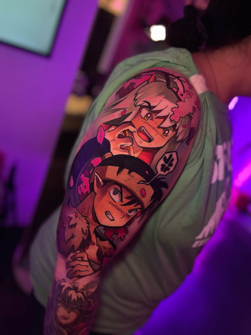 A close-up of a person's upper arm featuring a large, colorful anime-style tattoo with multiple characters. Done by Kelsie.